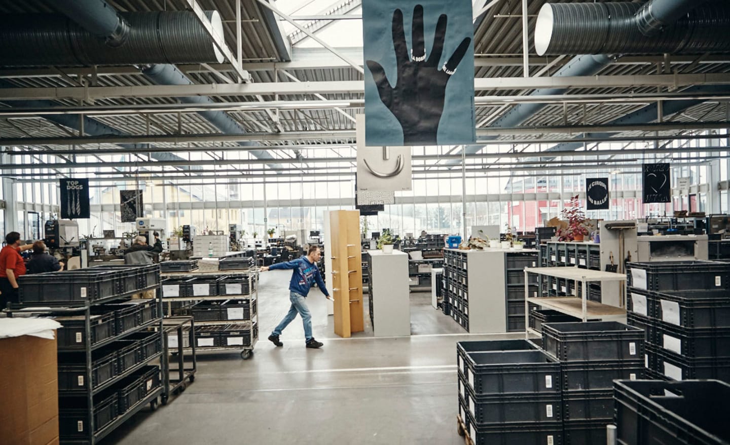 Production hall at the FSB manufacturing facility in Brakel, with employees, shelving systems, and transport carts.