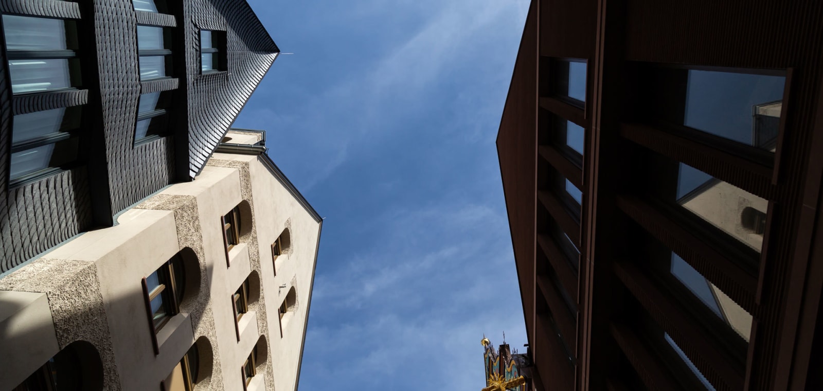 Upward view between historic and modern buildings in Frankfurt’s old town, with blue sky and a glimpse of a church tower