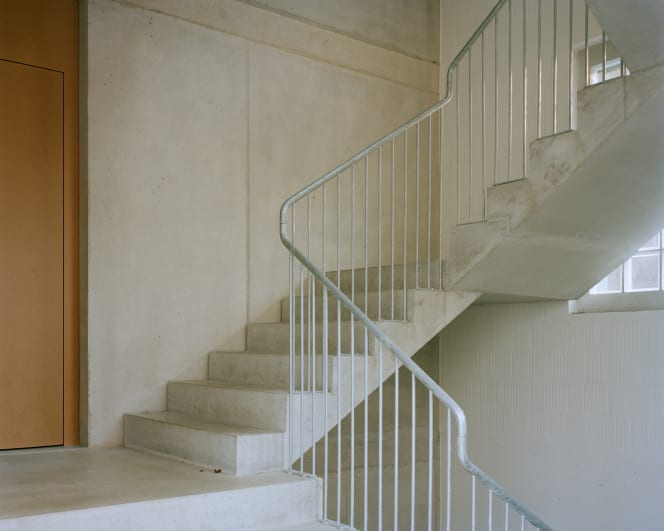Treppenhaus mit Sichtbeton, hellgrauem Metallgeländer und präzise geführter Treppe im Mehrfamilienhaus St. Gallen