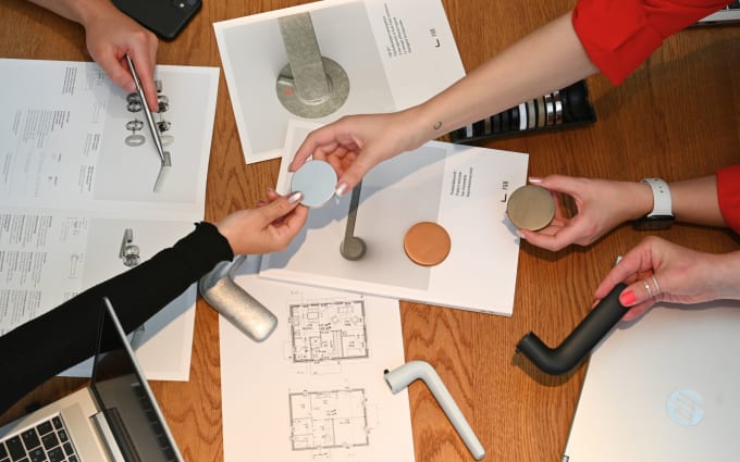 Meeting, in dem sich über Farbmuster eines Türdrückers von FSB unterhalten wird. Auf dem Tisch sind Hände, verschiedene Türdrücker und Produktbroschüren.