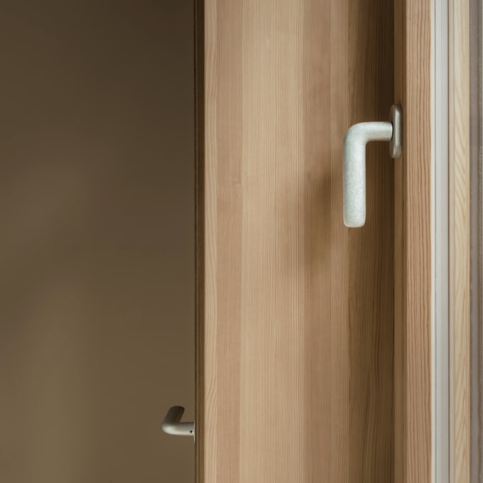 Nahaufnahme des Fenstergriff FSB 1292 in der Oberfläche Aluminium Pure senkrecht montiert in der ernst cave Weinbar in Berlin. Weiter entfernt ist auch der Türdrücker FSB 1292 in der selben Oberfläche zu sehen. Beide Beschläge kontrastieren mit der warmen Holzverkleidung der Bar.