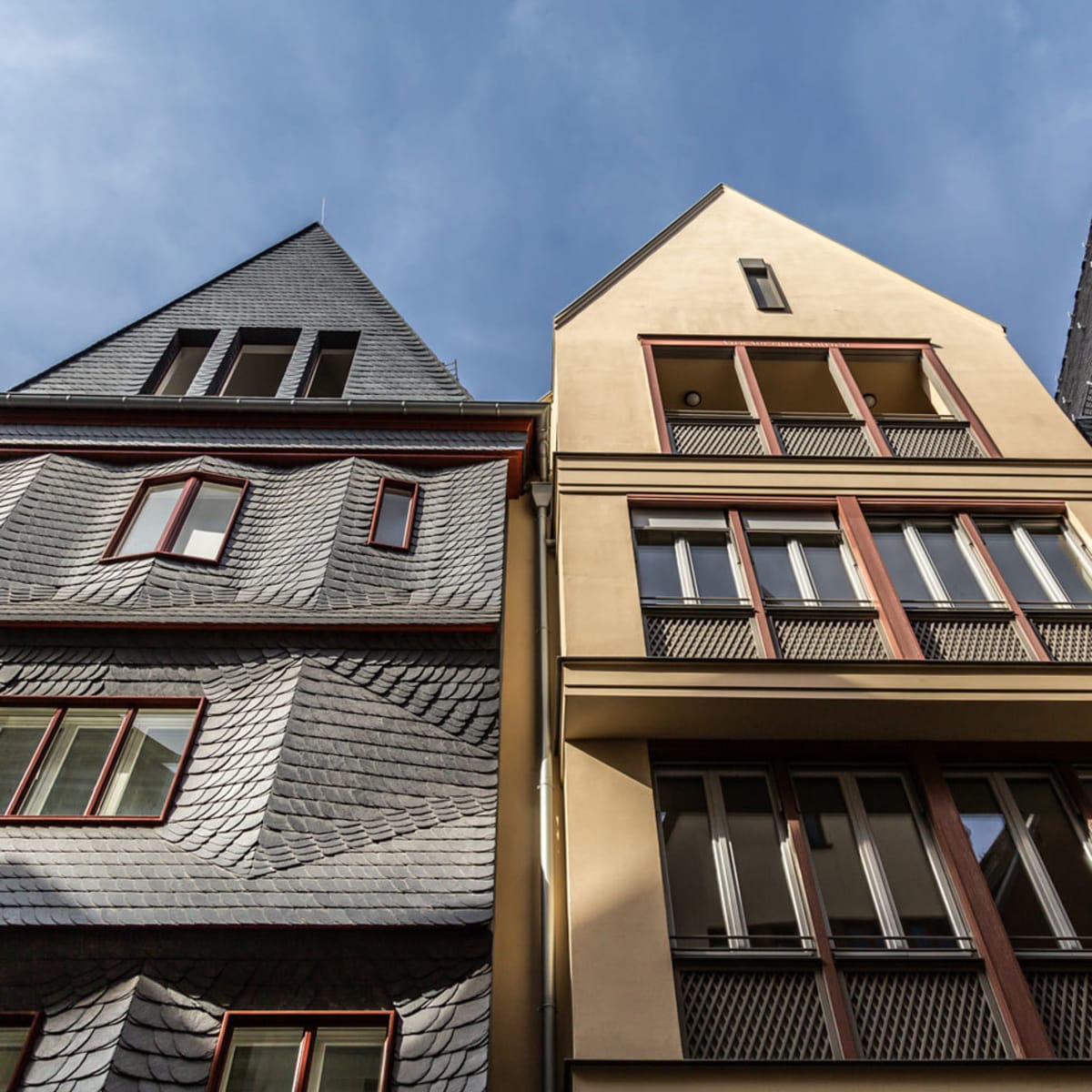 Fassadenansicht moderner Häuser in der neuen Frankfurter Altstadt zwischen Dom und Römer, mit schiefergedeckten Dächern und klaren geometrischen Formen unter blauem Himmel