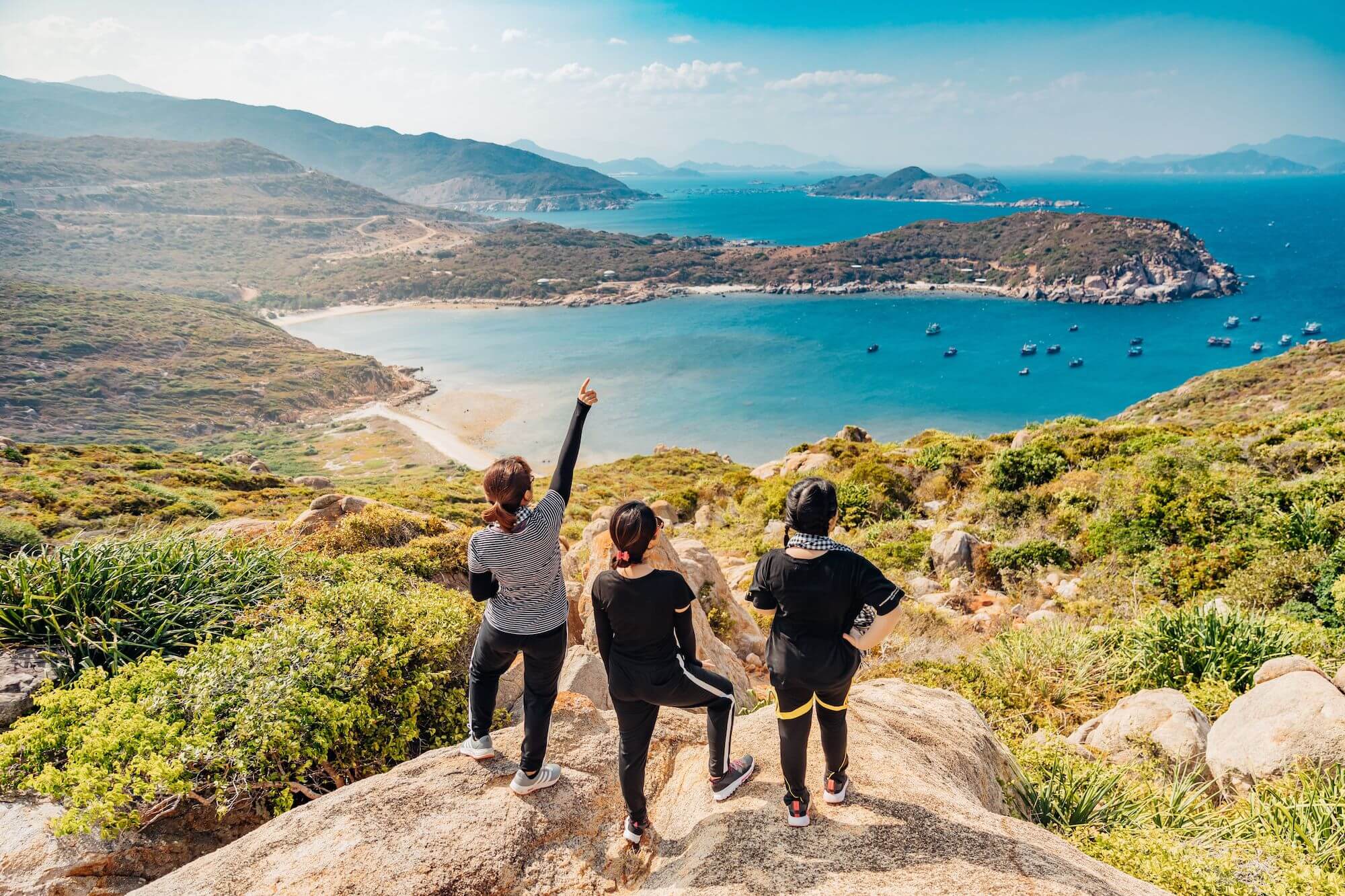 three people stood on top of a hill overlooking a blue lagoon and hillside