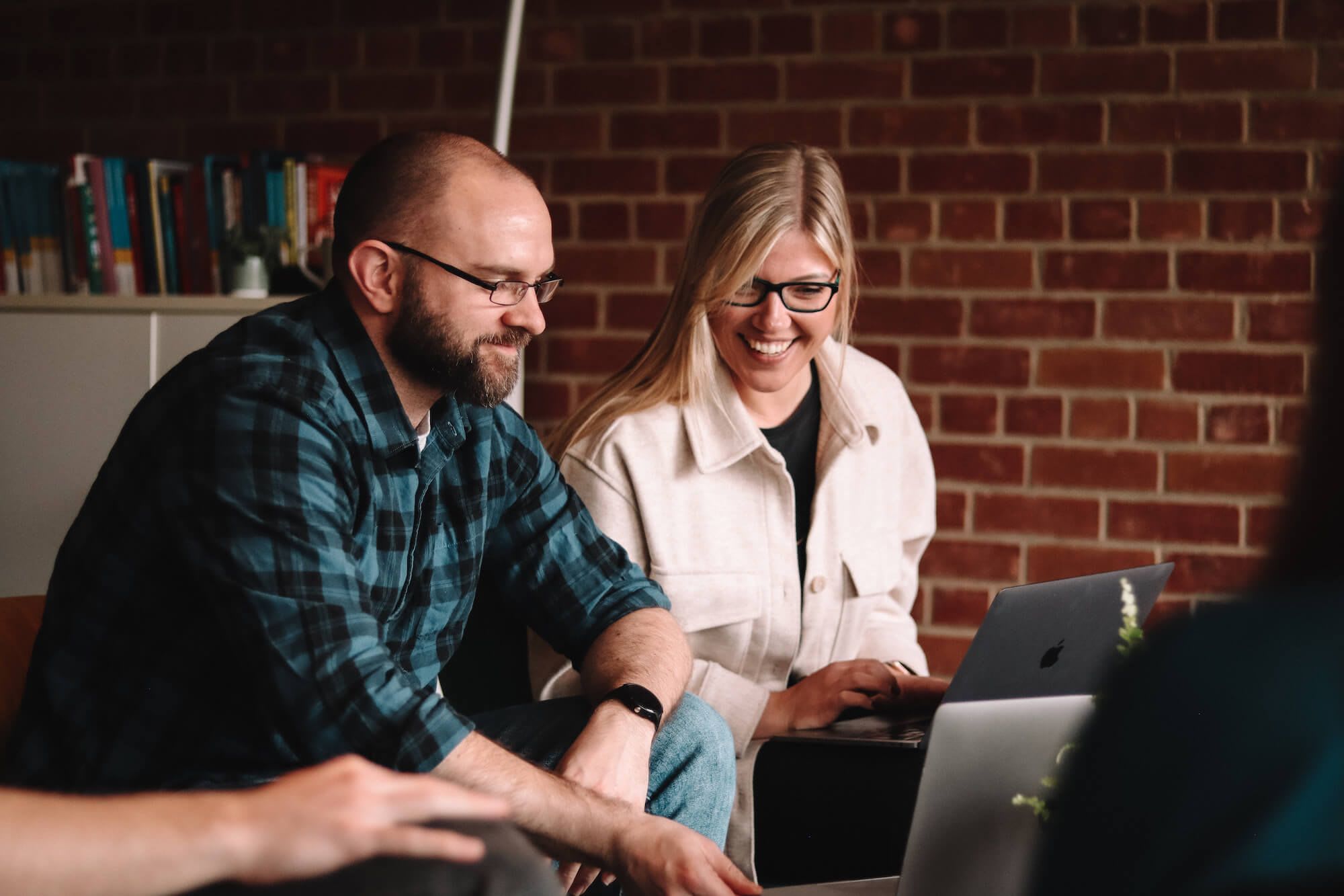 Two people sat together smiling and looking at laptops.