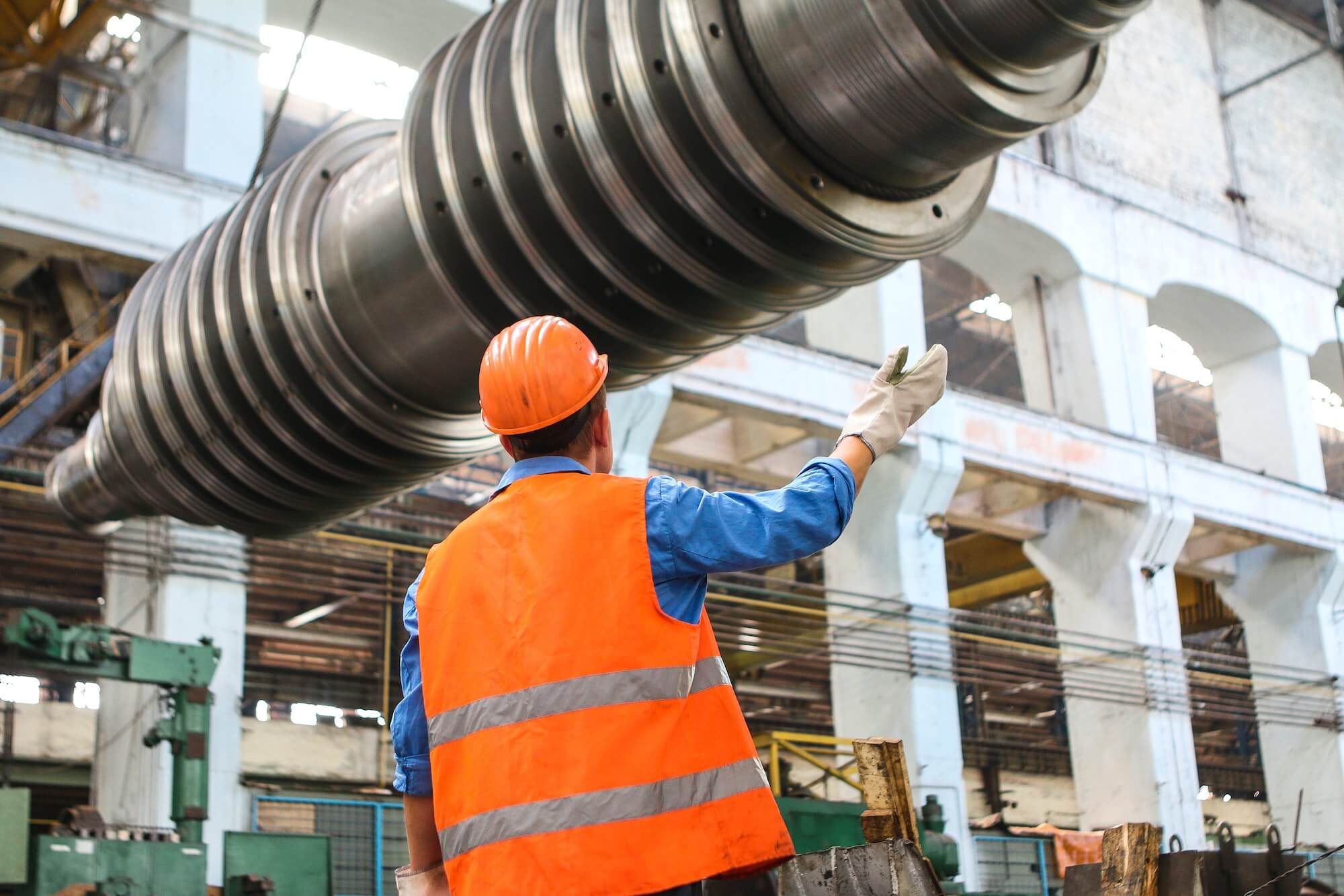 Person in a hard hat and fluorescent jacket directing a large piece of metal down from a crane on a building site.