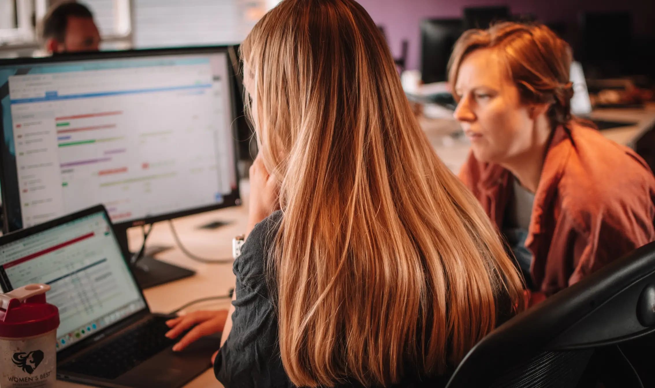 two people sat looking at computer screens and discussing work