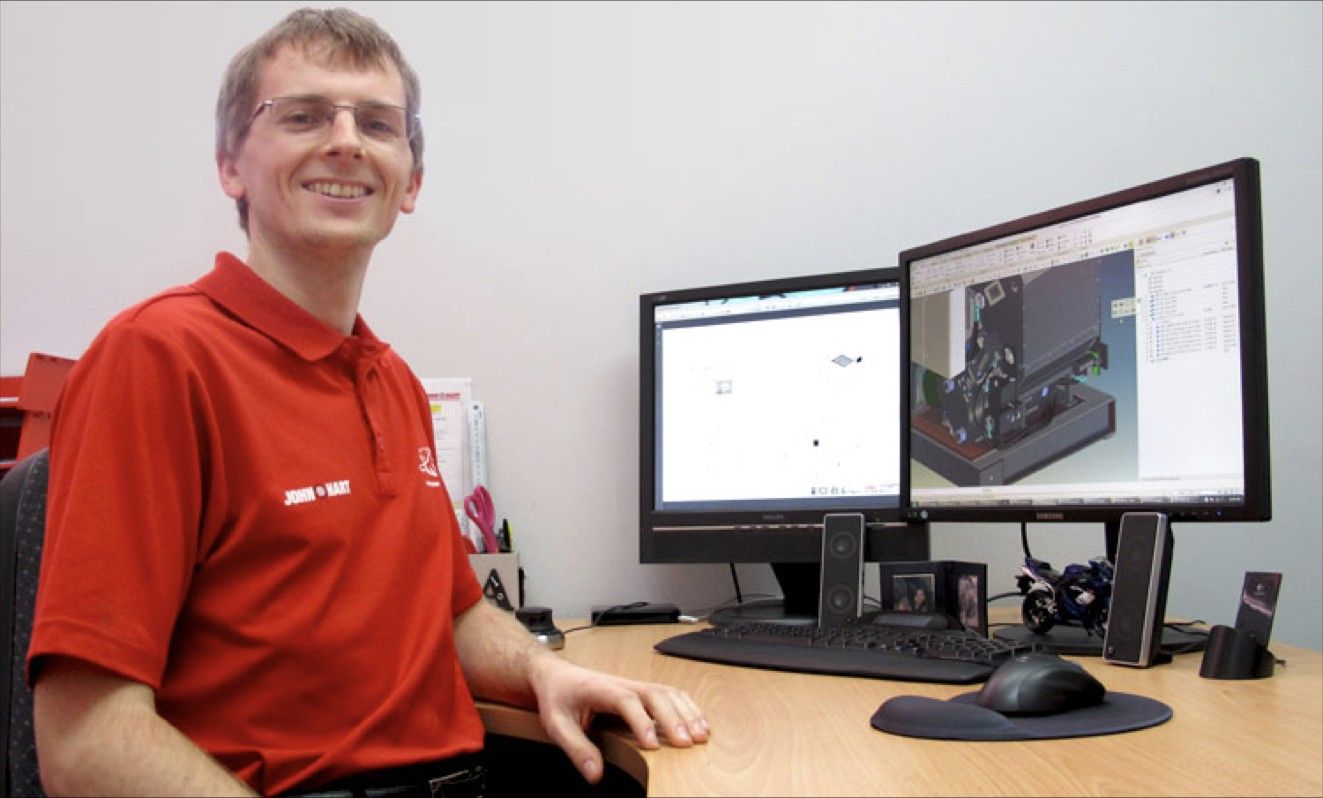 Person smiling at the camera sat at a desk looking at components