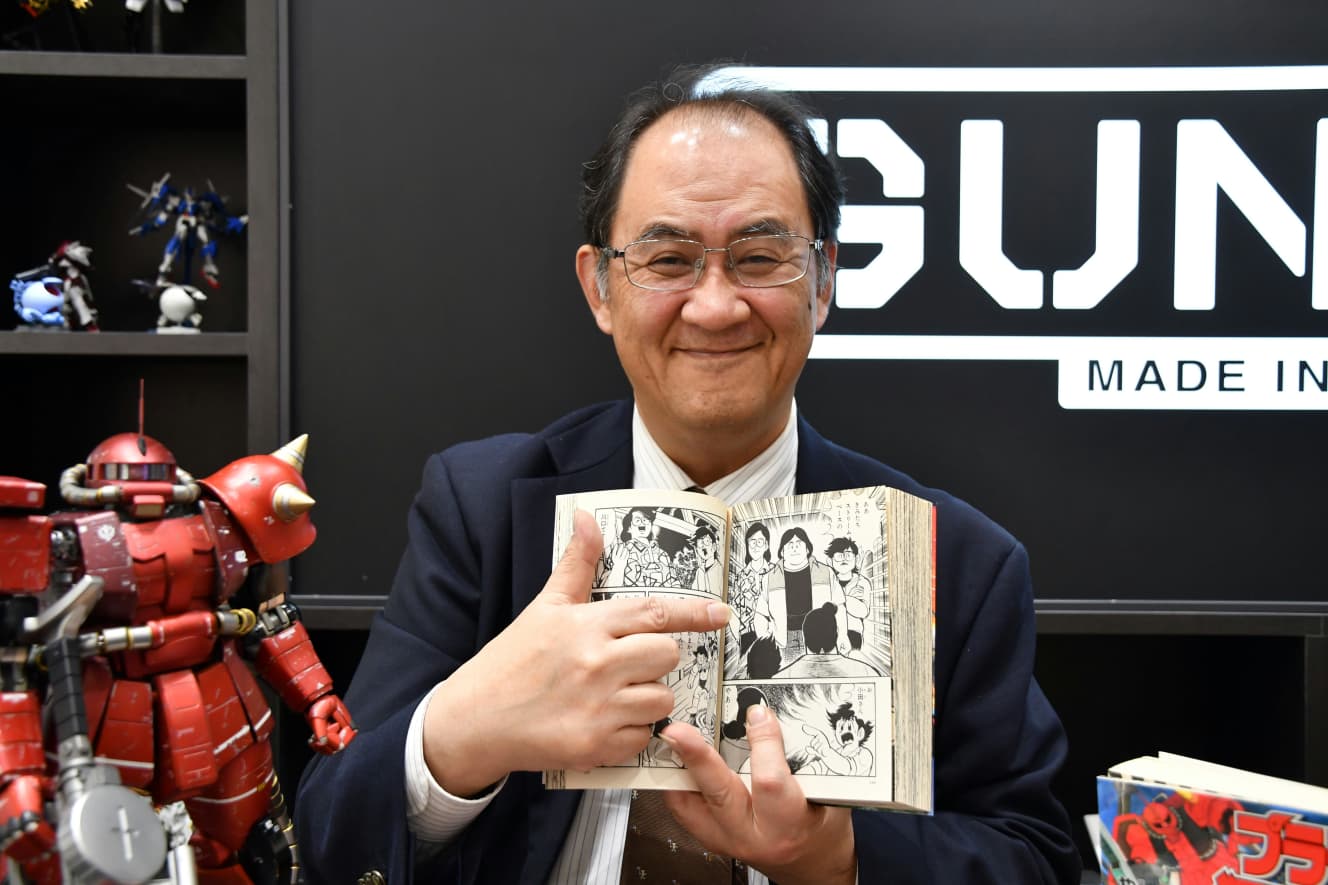 「プラモ狂四郎」に登場する大学生だった自分を指さす川口名人。「プラモ狂四郎」の中で、大学生だった川口青年は、四郎らガンプラ少年たちに「プラモの改造は外見だけじゃだめなんだぜ」と“極意”を伝授している。(写真:竹内みちまろ)
