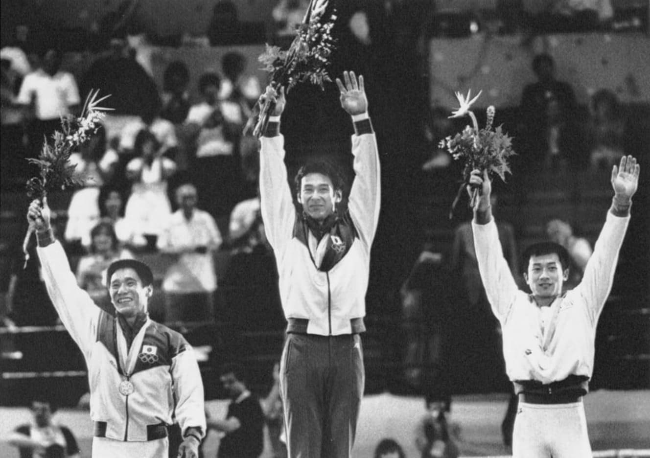 1984年ロサンゼルスオリンピック体操男子種目別の鉄棒で優勝。表彰台で両手を上げる森末氏（写真中央）。「僕がオリンピックに出たころより、器具がとても進化している。当時はできなかった技が今できるのは、器具の進化も大きいと思います」（写真：共同通信）