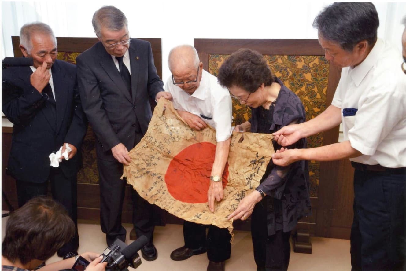 返還された旗を手にした日本の遺族たち。OBONソサエティの活動が広まるにつれ、メディアからも注目されるようになっていった