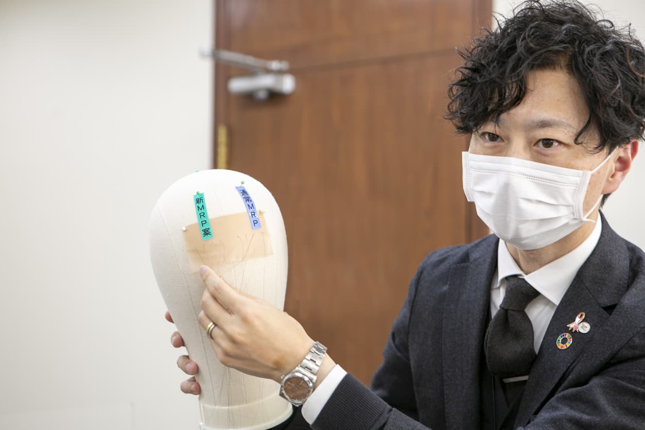 「自然」を追及して太さ0.06~0.07ミリの髪の毛を削った新技術を説明してくれた開発者の矢内さん。肉眼では全くその違いがわからないが…