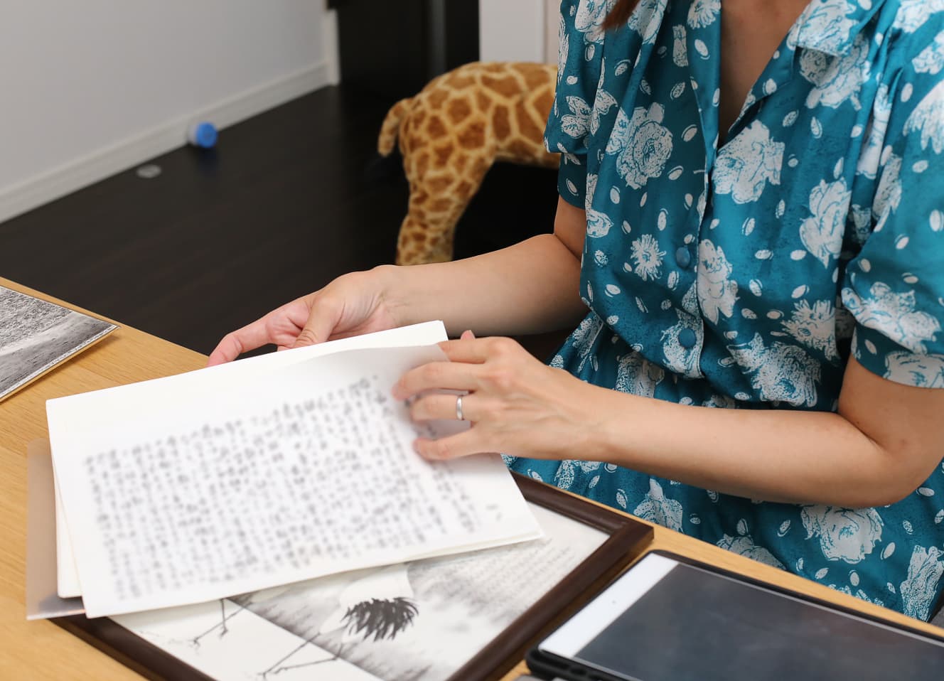 岡﨑の手記と絵を手に取材を受ける茜さん。保管する作品には１ｍ四方を超えるサイズのものもあるという