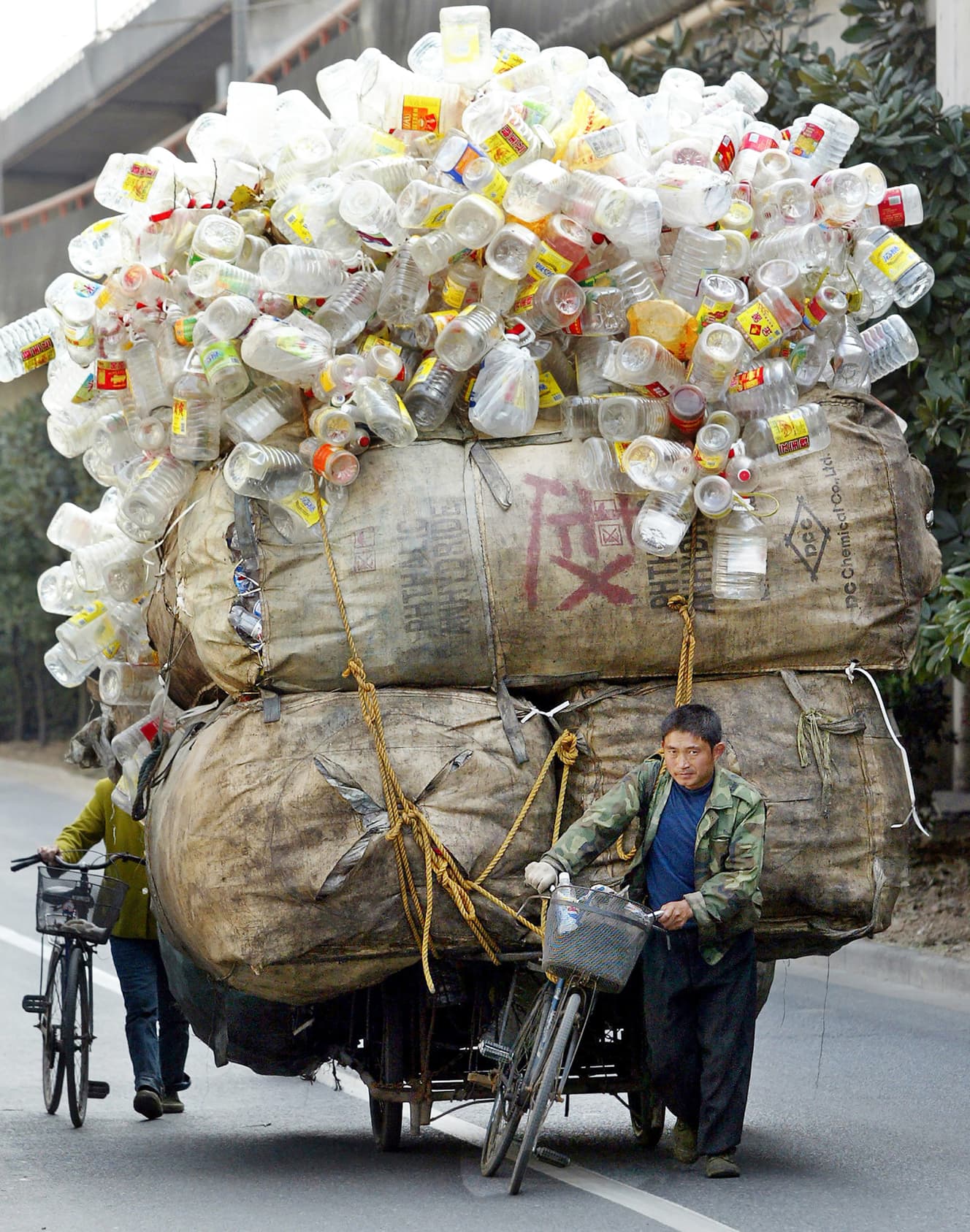 上海の路上で、大量のペットボトルと巨大なズダ袋を載せた荷台を引く中古の自転車と男性