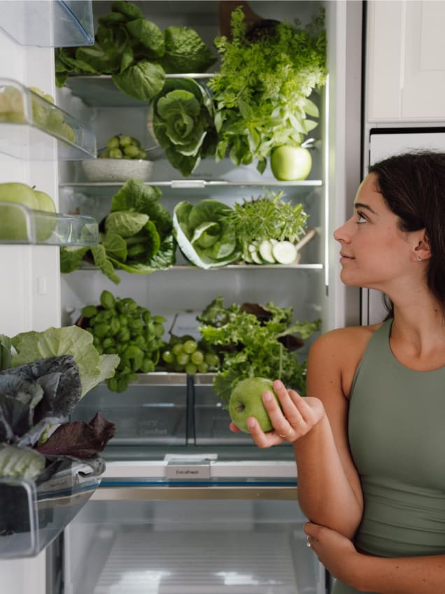 Mujer junto a nevera llena de verduras y fruta