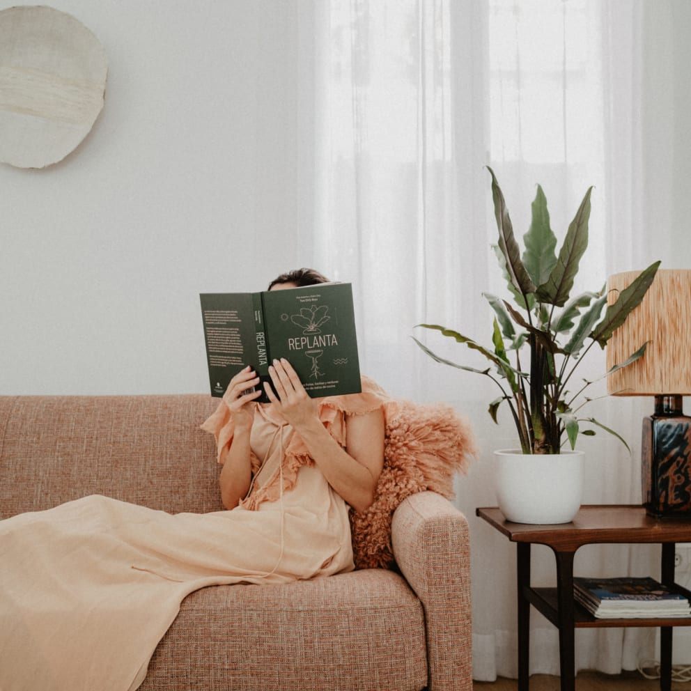 Persona sentada en sofá leyendo libro de plantas