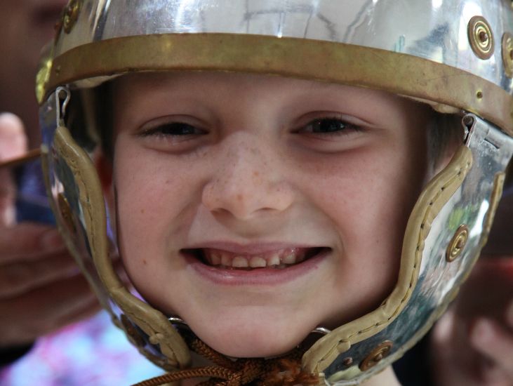 boy wearing a silver roman helmet smiles for the camera
