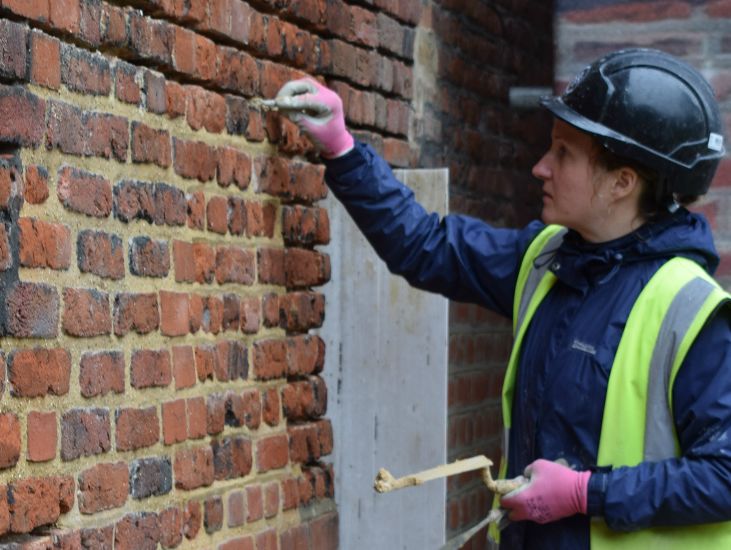 A bricklayer carefully putting mortar on a brick wall