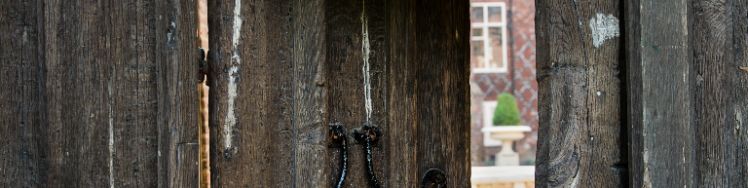 door in front wooden gate slightly open with glimpse of tudor courtyard through it
