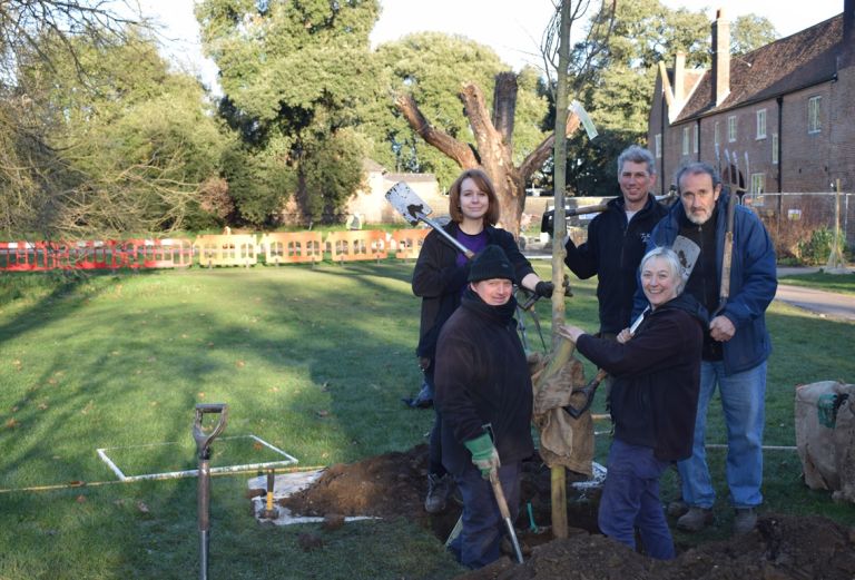 a group of five people stand next to a newly planted sapling
