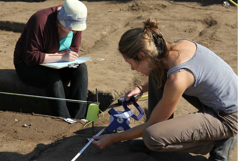 two archaeology volunteers measure a pit