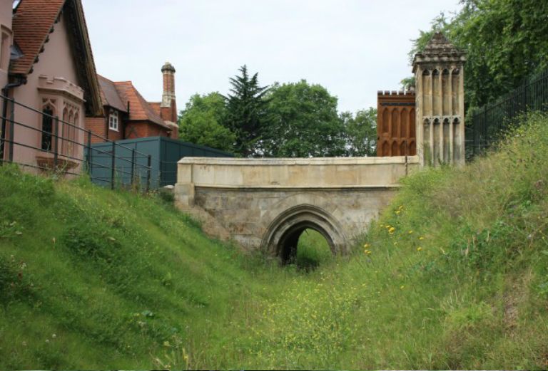 the moat with long grass and a stone bridge in the background