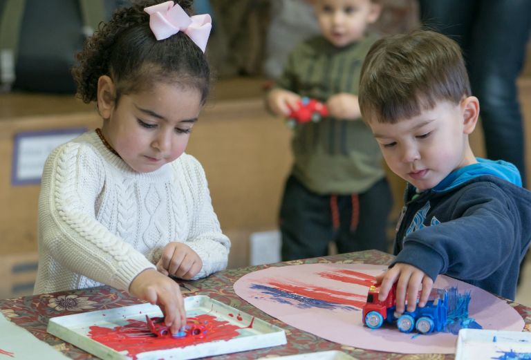 two young children play with cars and paint