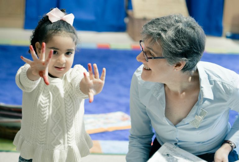 a woman smiles at a child holding her hands up that are covered in paint