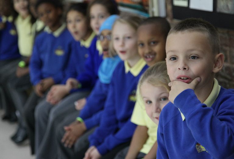 a group of school children dressed in blue sit and smile