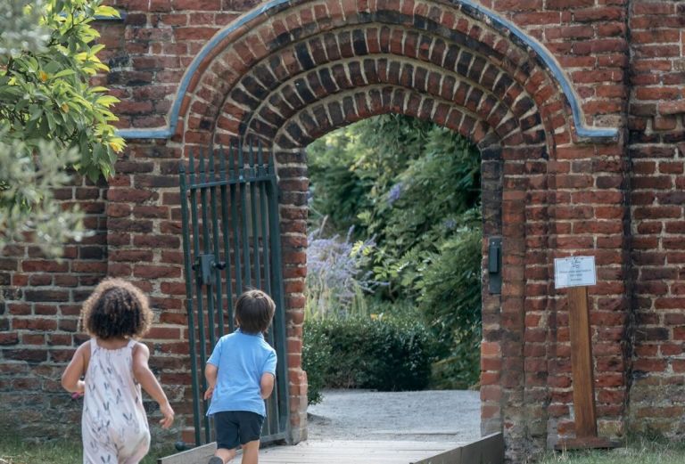 two children run towards the brick Tudor gate to the walled garden