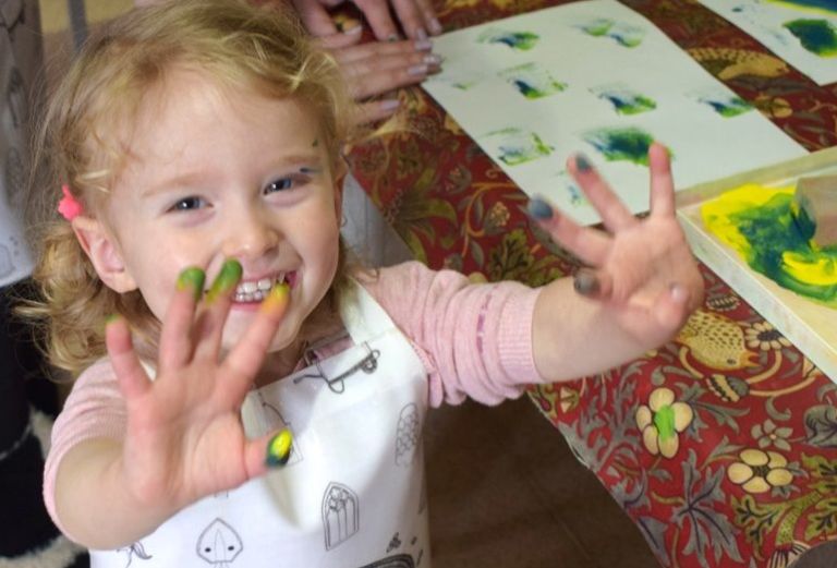 little girl shows off her hands covered in paint from a craft activity