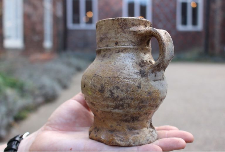 A clay pot with a handle rests on a hand