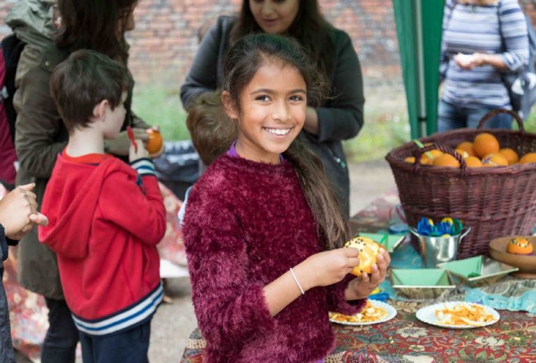 A girl smiles as she puts cloves into an orange