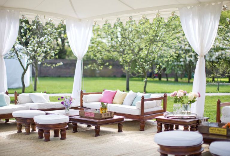 white sofas and chairs under a white tent in the garden