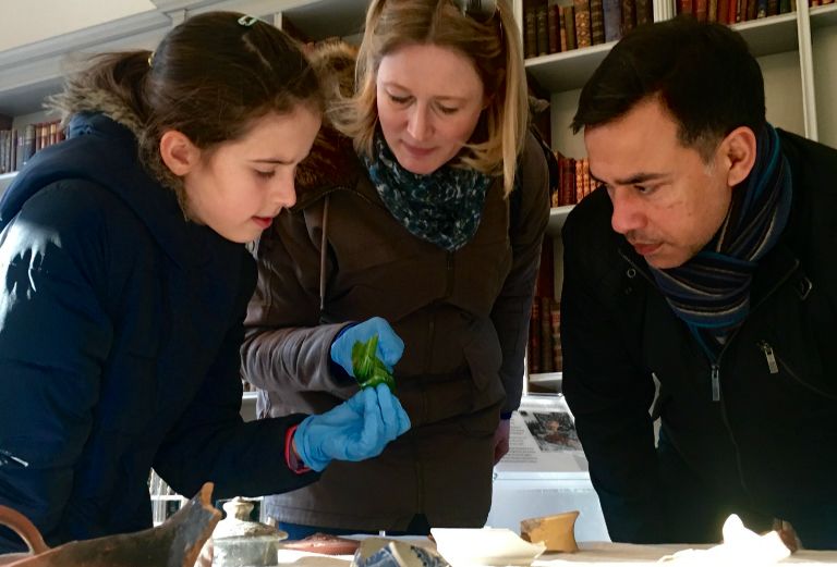 teenage girl, woman and man examine a glass artefact