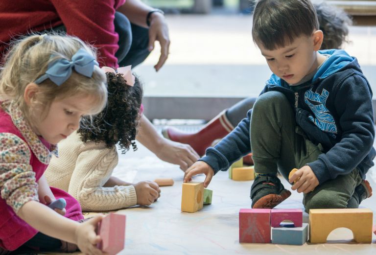 two little girls and a little boy play with blocks on the floor