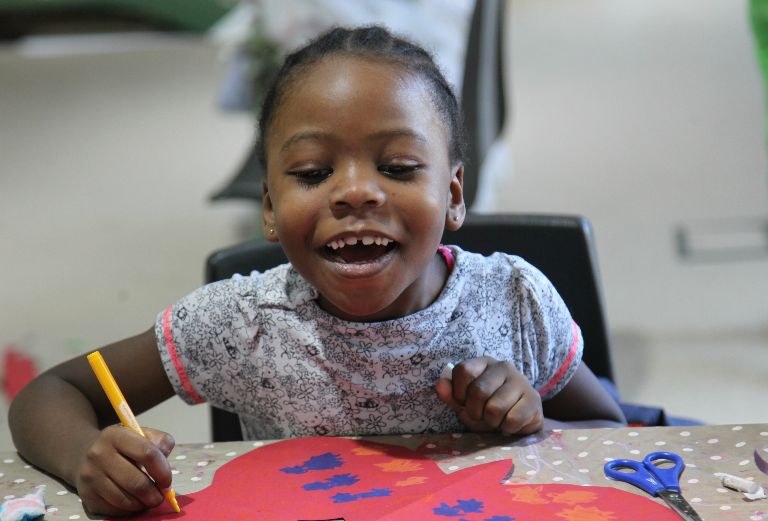 little girl smiles at the red paper butterfly she is painting in bright colours