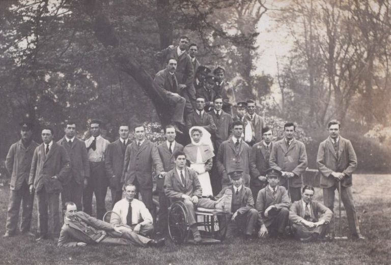 A photograph of a group of people, many in soldiers uniform standing by and in a tree