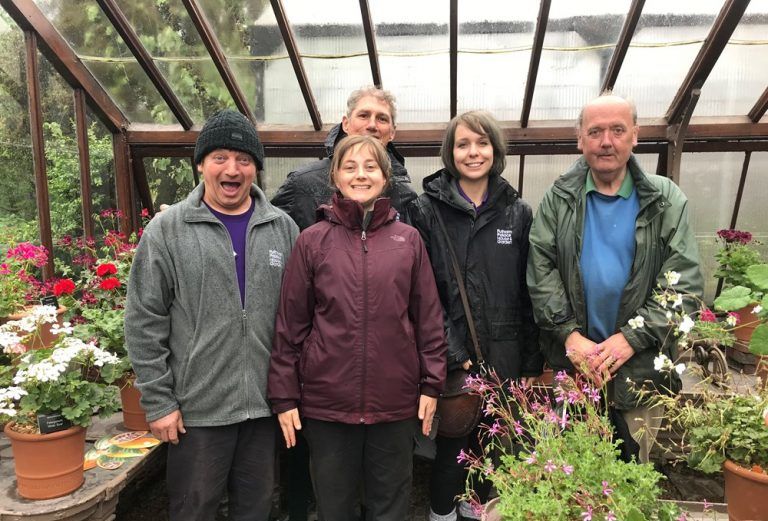 The Fulham Palace garden team, five team members smile, they are standing in a greenhouse surrounded by plants