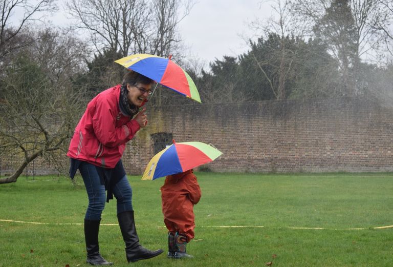 A woman and child are standing together holding umbrellas in the rain in Fulham Palace gardens. They are enjoying a fun moment together.