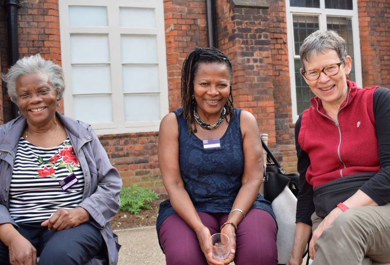Three women sit in a courtyard. All are smiling at the camera