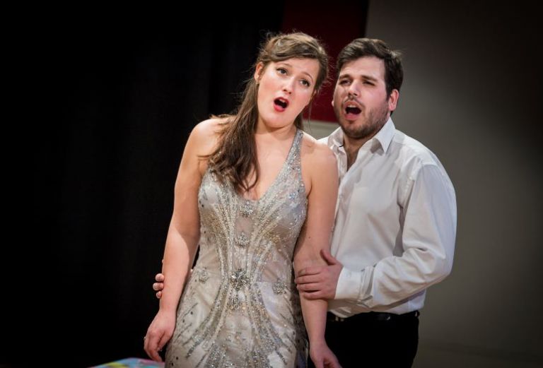 Young female and male opera singers dressed in evening wear are performing. They are singing together intimately.