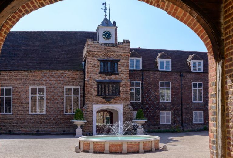 looking into a courtyard from underneath an arch on a sunny day with a fountain in the center