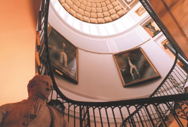 looking up an umbrella shaped staircase with large painting on the wall and a statue in the bottom left hand corner