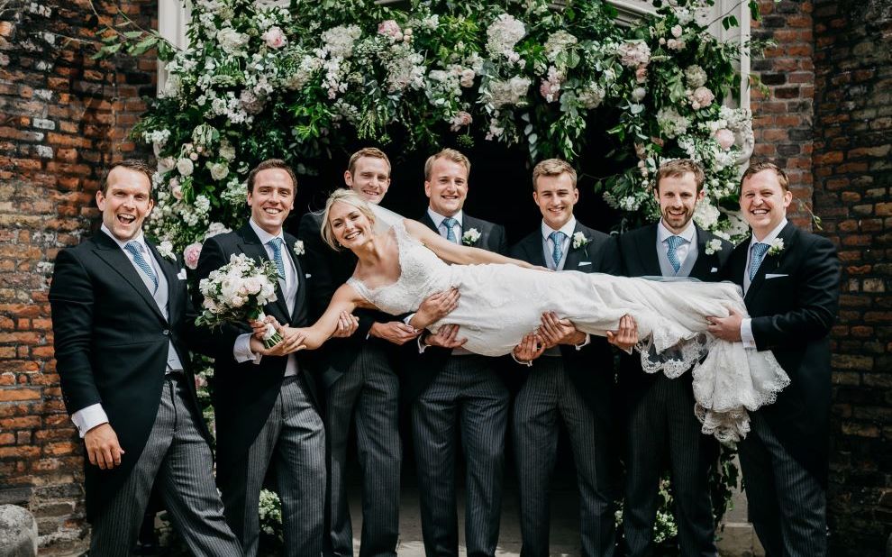 woman in a wedding dress is held up by a group of men in suits