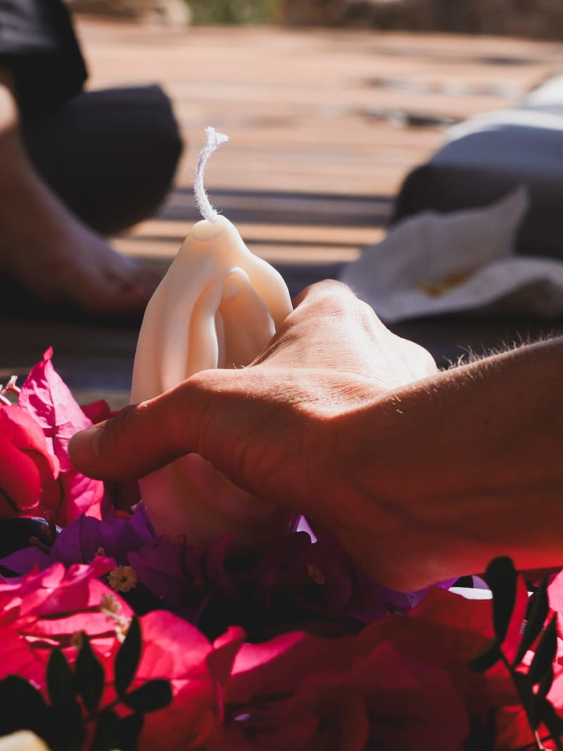 Een close-up van een hand die tijdens een Yoni Retreat een kaars in de vorm van een Yoni op rode bloemblaadjes plaatst.
