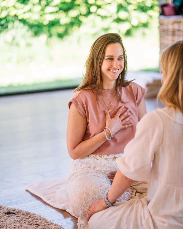 Frontaal beeld van Griet Alice die tijdens een yoni retreat tegenover een vrouw zit. Ze lijken te delen, ze heeft haar hand op haar hart.