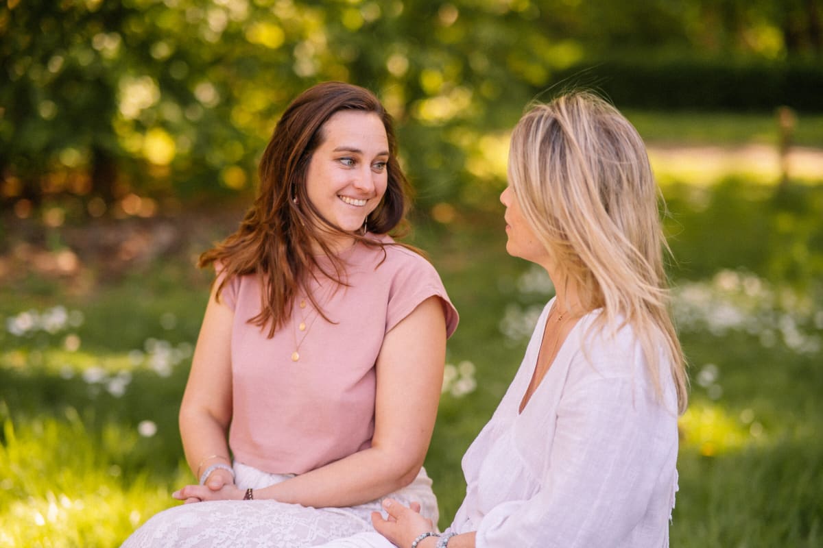 Twee vrouwen in een open gesprek in het gras — vrouwelijk leiderschap begint bij echte verbinding