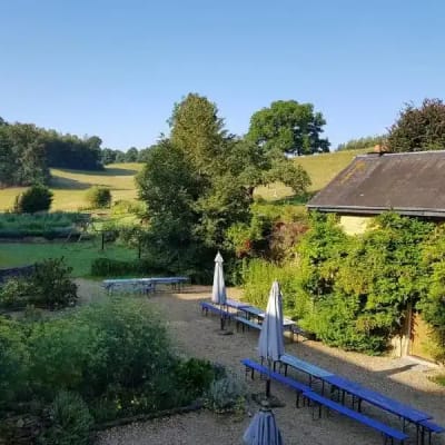 Een overzichtsshot van de hoeve van Orval, waar het Singles Retreat plaatsvindt. Je ziet de binnenkoer met gesloten parasols. Bomen en heuvels op de achtergrond.
