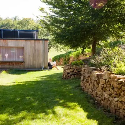 Een zonnig beeld van een stuk tuin en de tempelzaal. Een deelnemer aan het singles retreat zit in de zon te lezen.