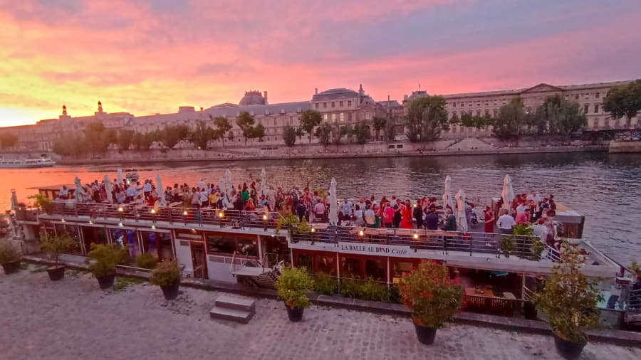 une péniche à quai avec des personnes qui célèbrent au coucher de soleil à paris